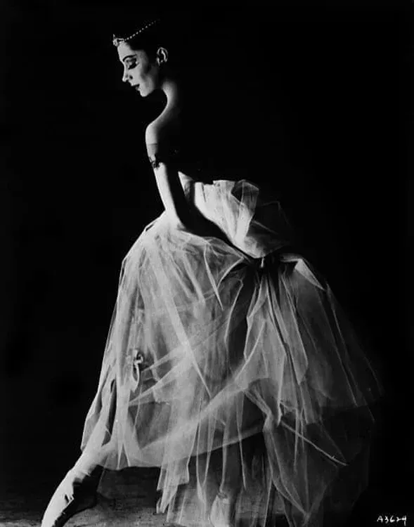 A ballerina is sitting on the floor in a black and white photo.