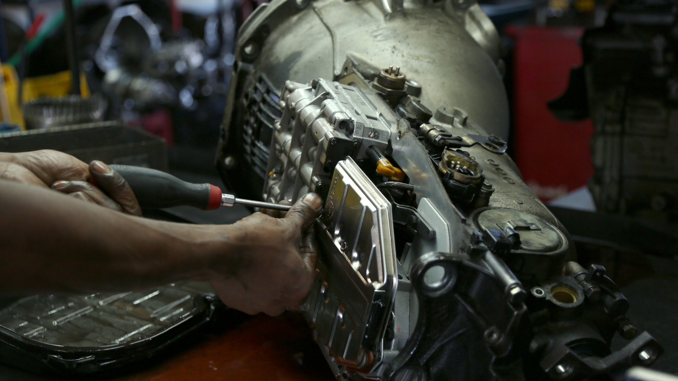 Person using a screwdriver to remove a plate from a vehicle transmission in a workshop.