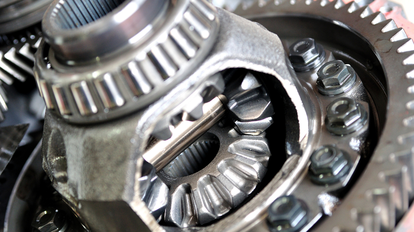 Close-up of a car differential, showing gears, bearings, and bolts; steel and silver tones.