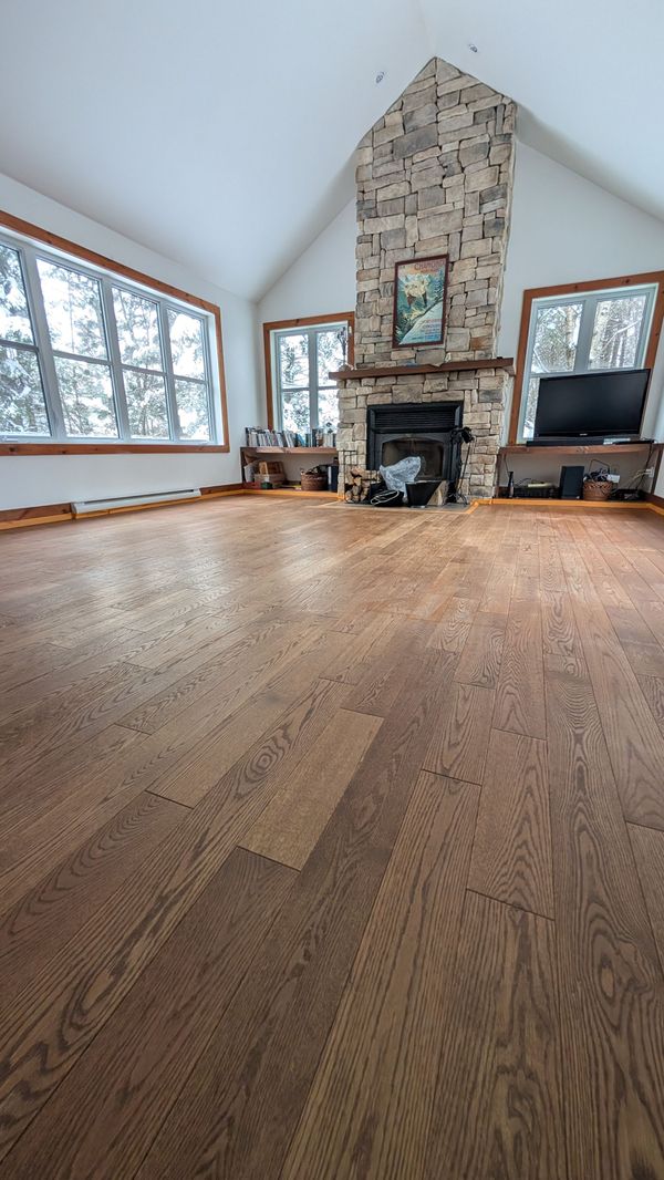 Salon spacieux avec parquet, cheminée en pierre et grandes fenêtres donnant sur la neige à l'extérieur.