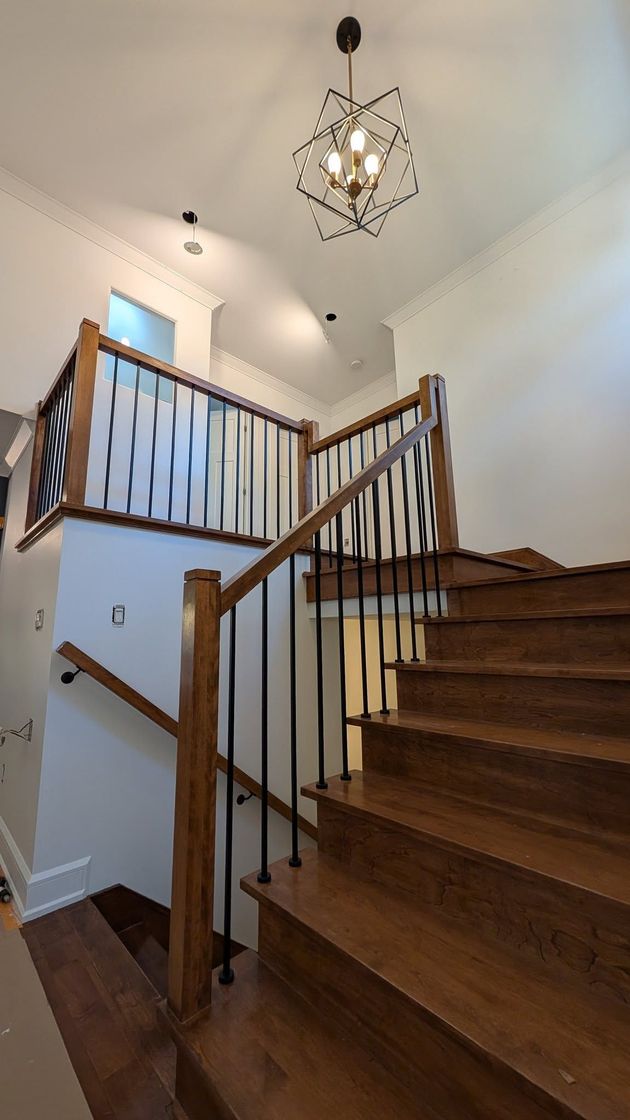 Un escalier en bois avec une rampe sombre, un lustre et un mur blanc.