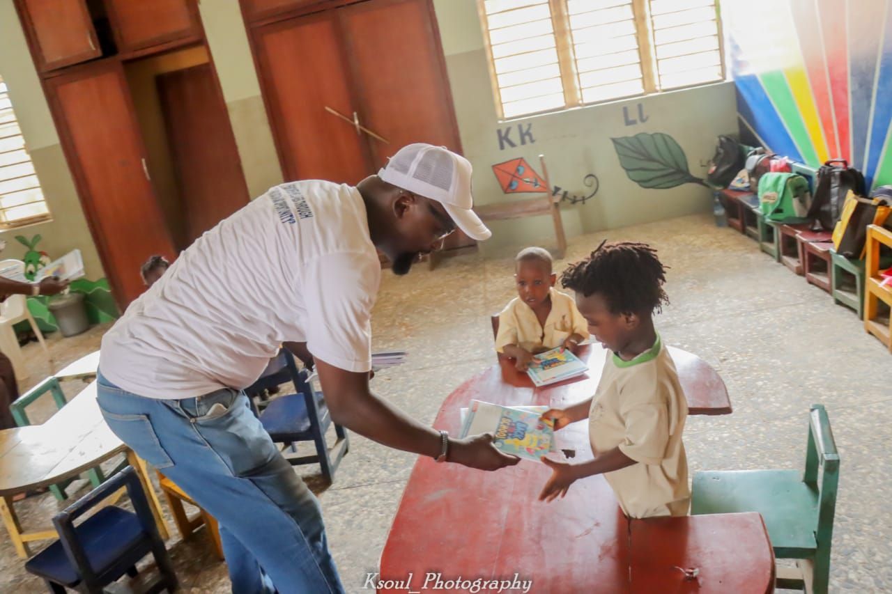 a man is giving a book to a child in a classroom .