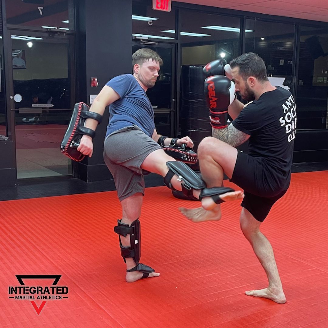 Two men are kickboxing on a red mat in a gym.