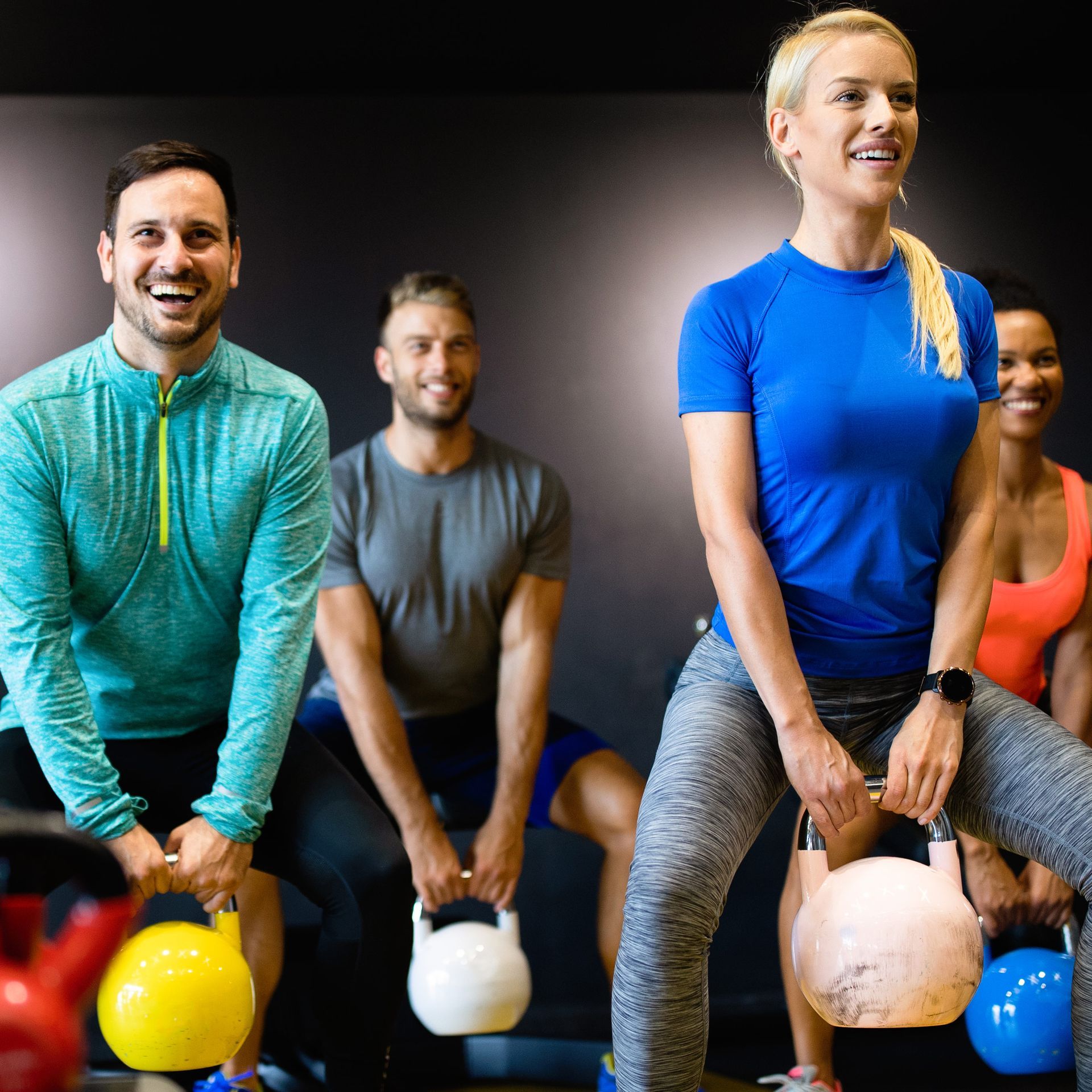A group of people are squatting with kettlebells in a gym.