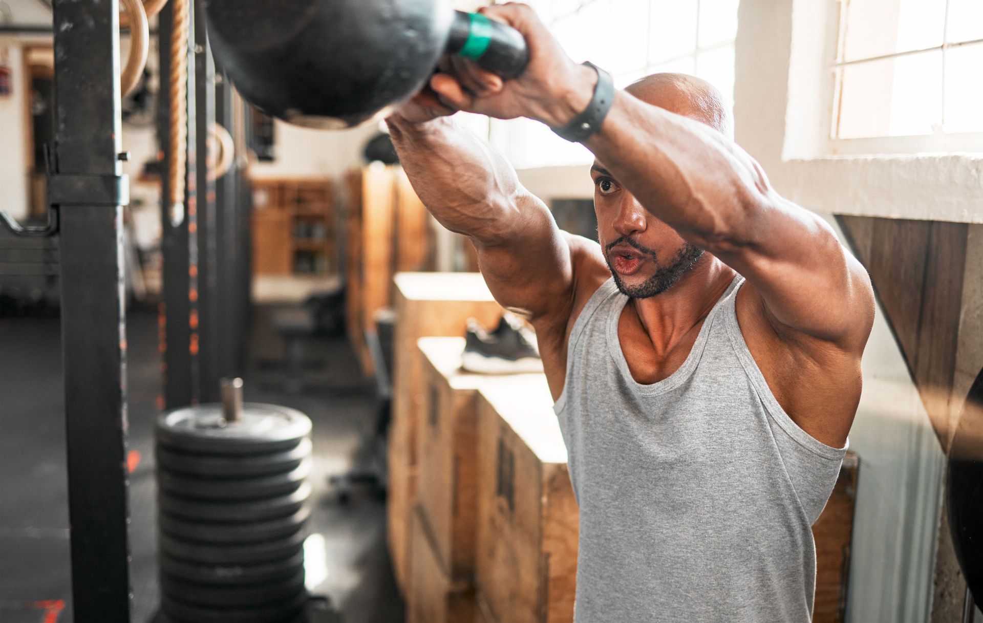 A man is lifting a kettlebell over his head in a gym.