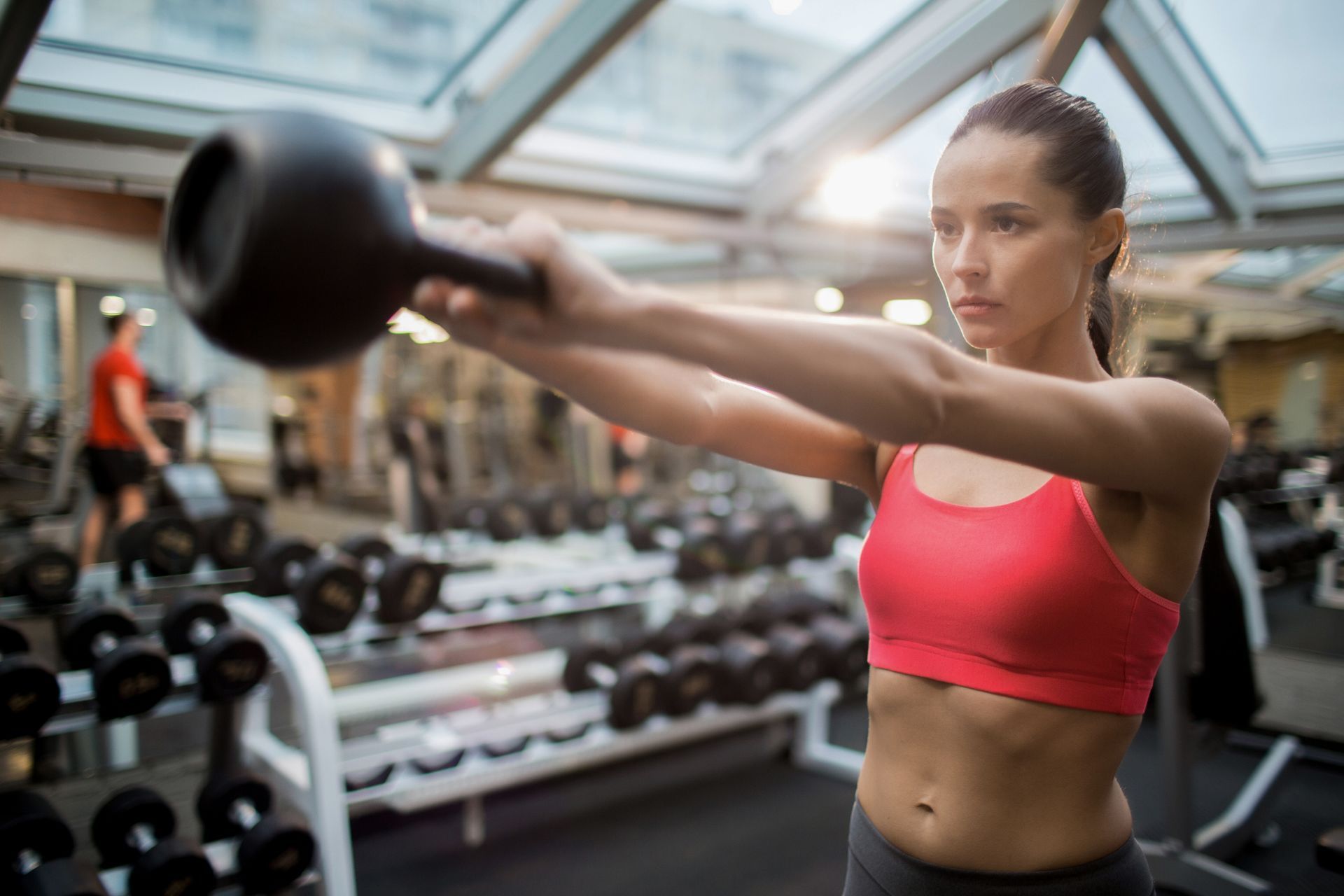 A woman is lifting a kettlebell over her head in a gym.