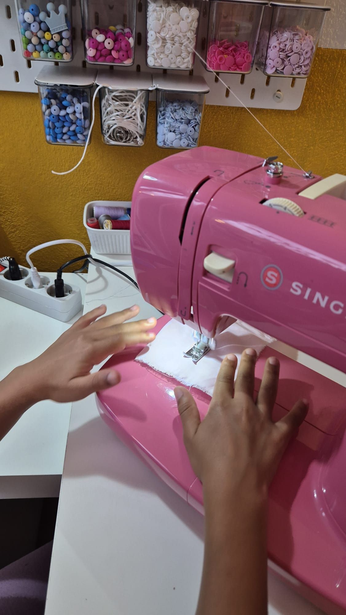 Uma pessoa está usando uma máquina de costura rosa em uma mesa.