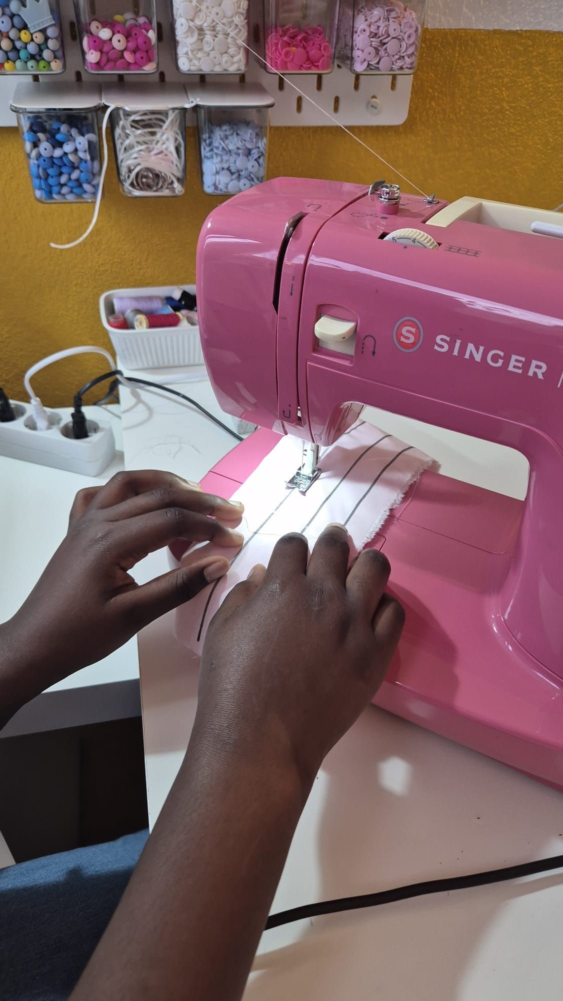 Uma pessoa está usando uma máquina de costura Singer rosa em uma mesa.
