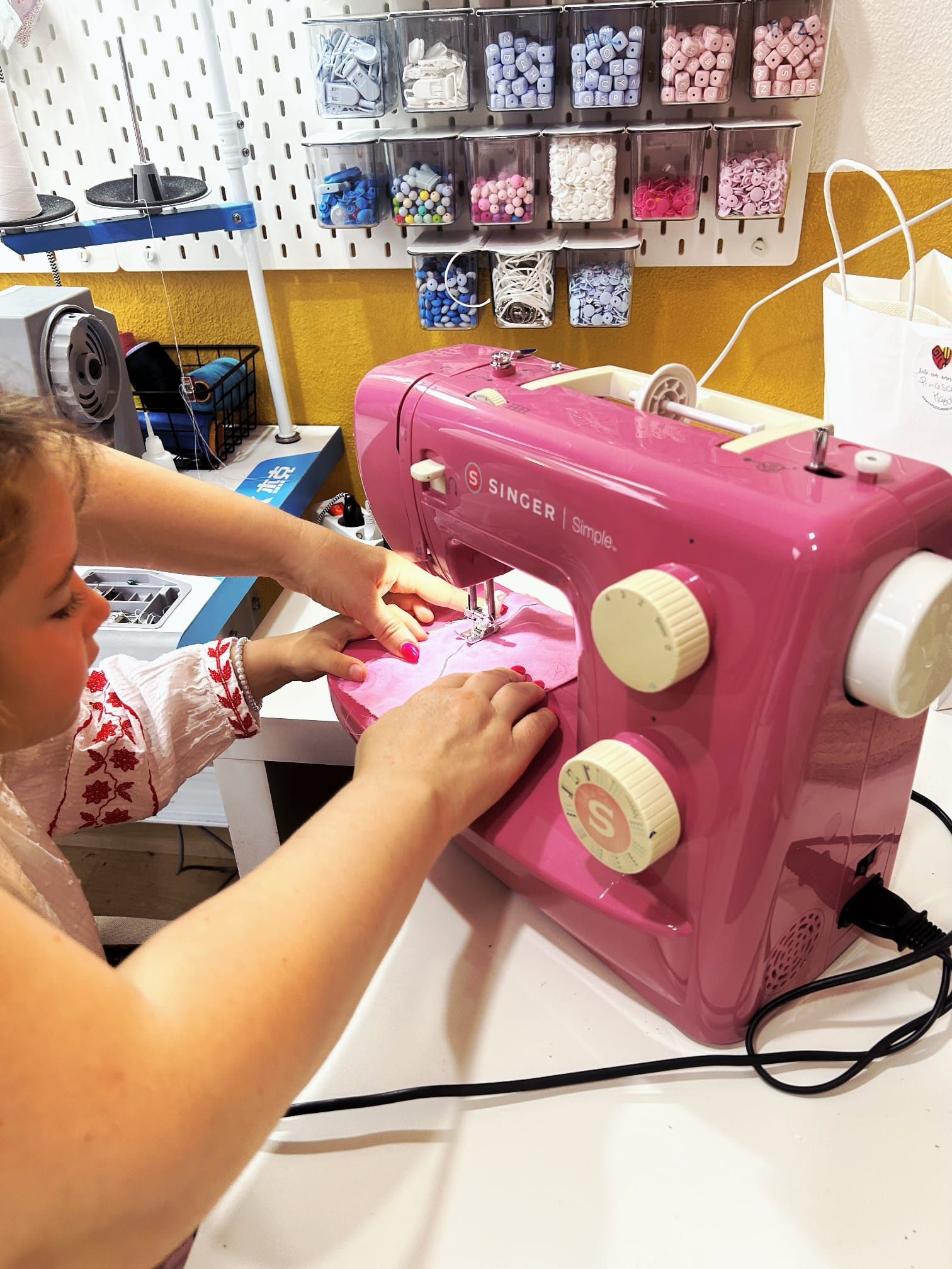 Uma mulher está usando uma máquina de costura rosa em uma mesa.
