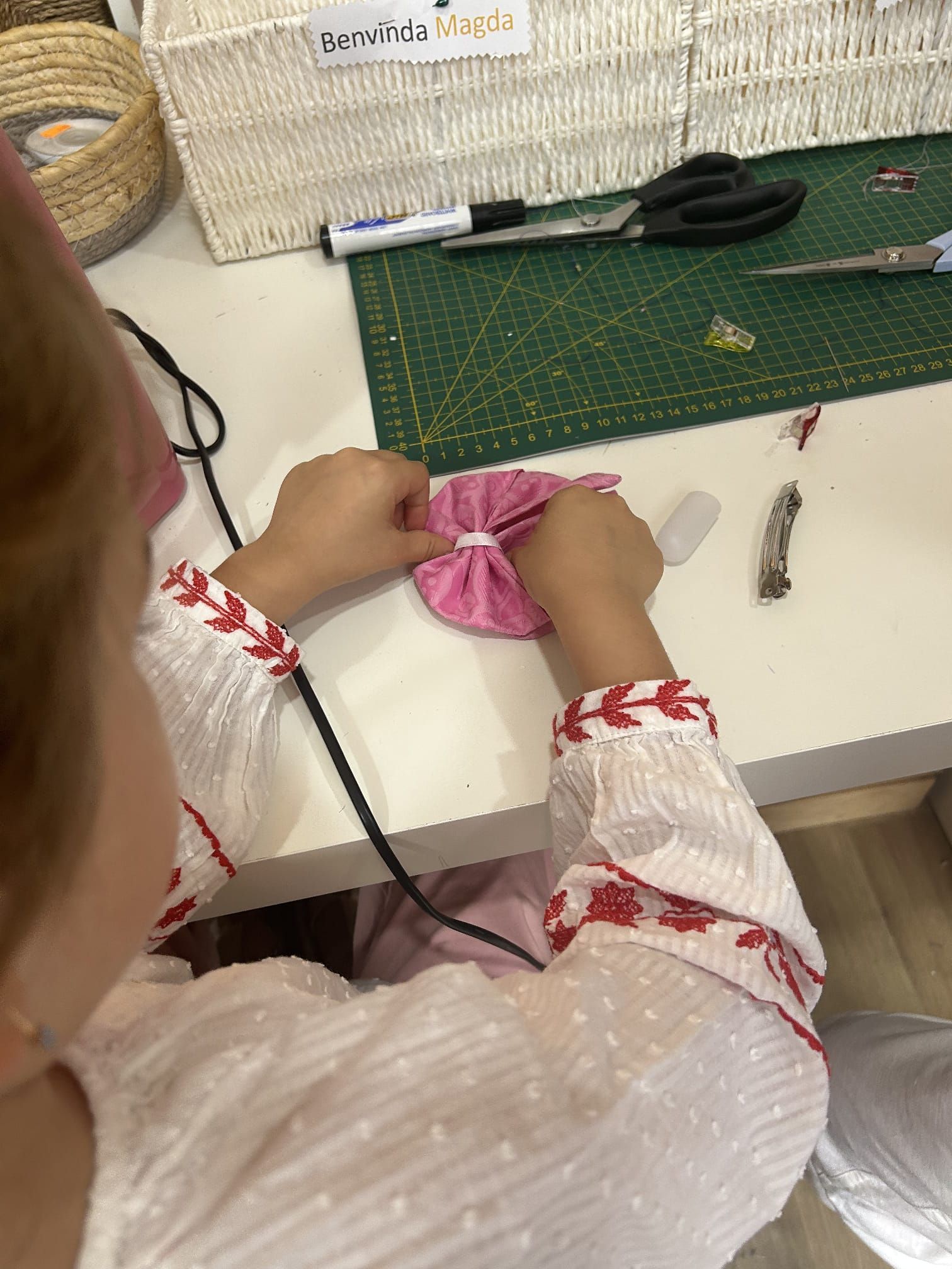 Uma menina está sentada à mesa fazendo uma flor.