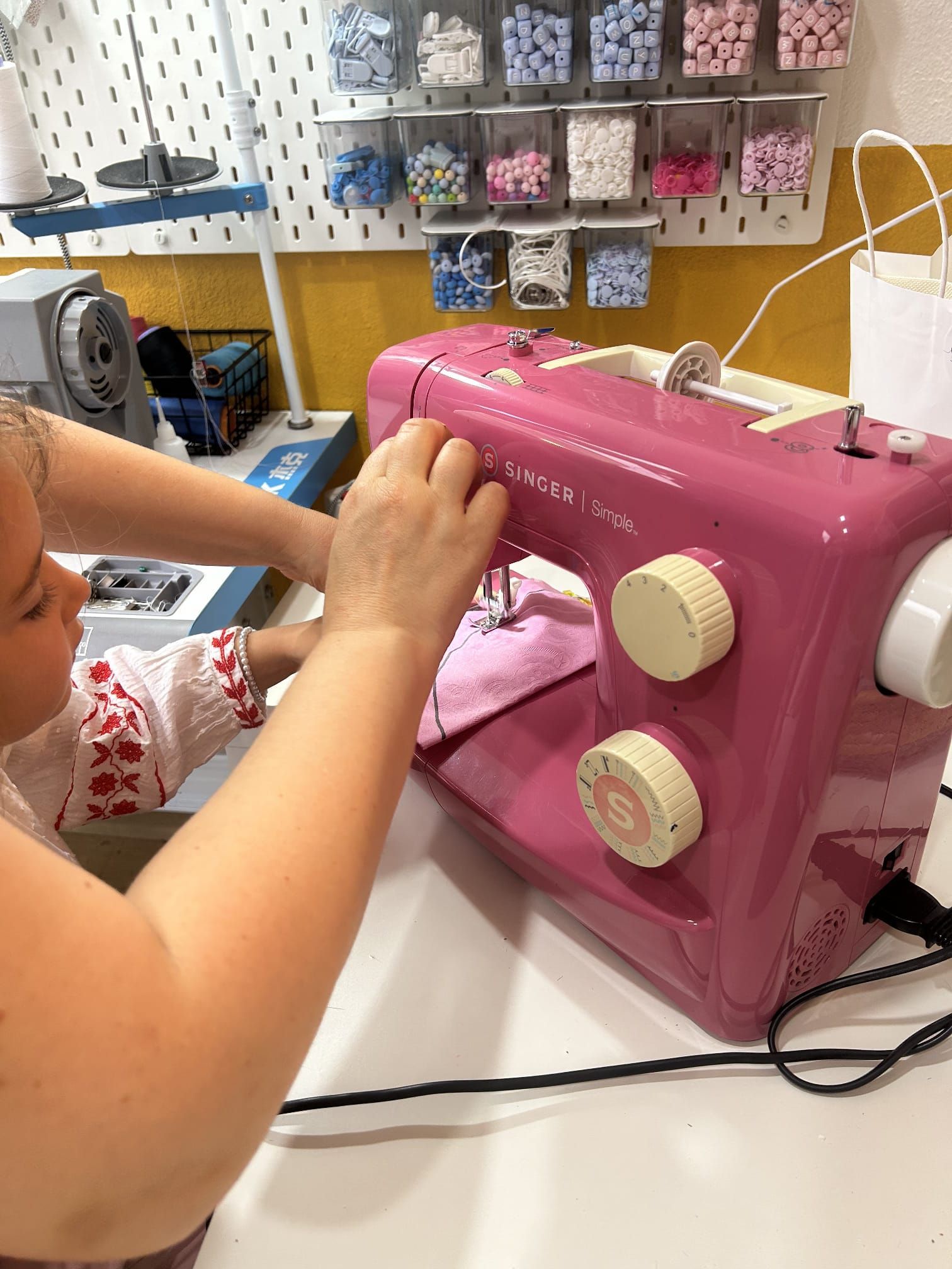 Uma garotinha está usando uma máquina de costura rosa.