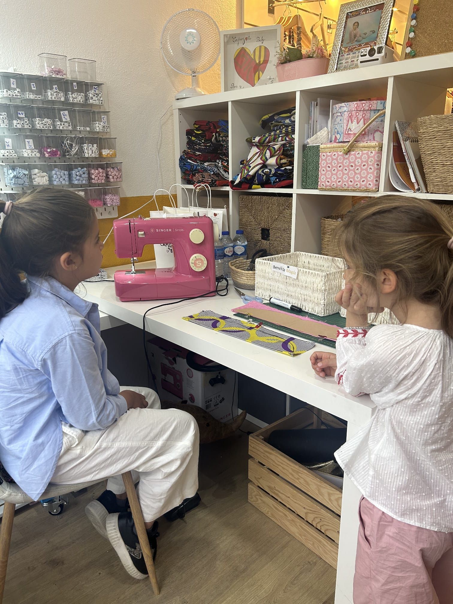Duas meninas estão sentadas à mesa com uma máquina de costura.