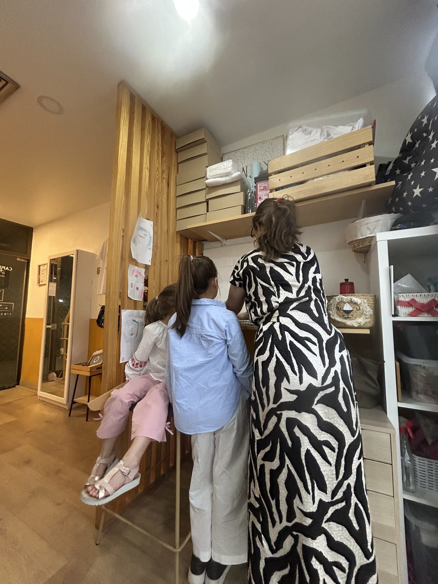 Uma mulher com um vestido estampado de zebra está parada ao lado de duas crianças em uma sala.