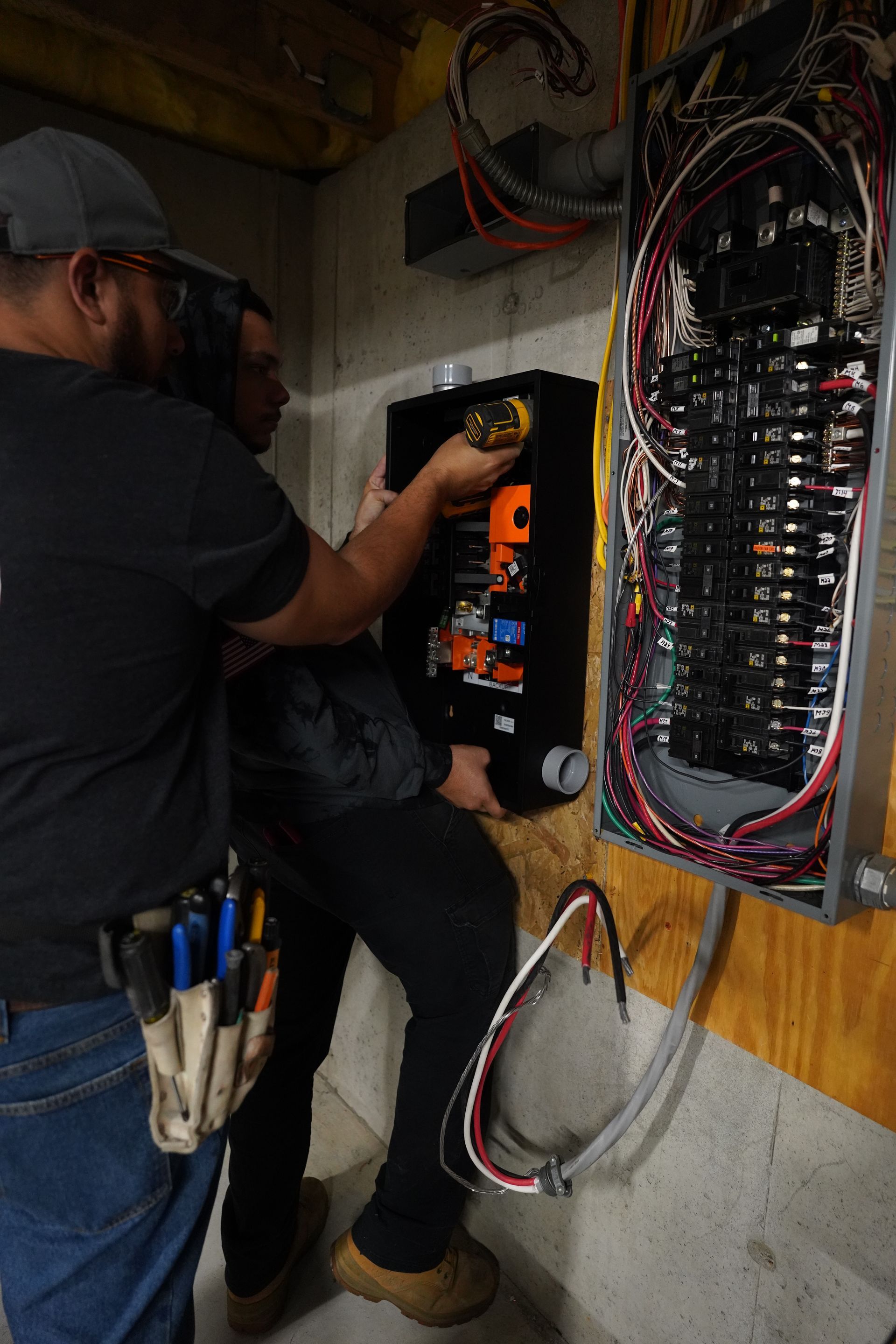 two men are working on an electrical box in a basement .