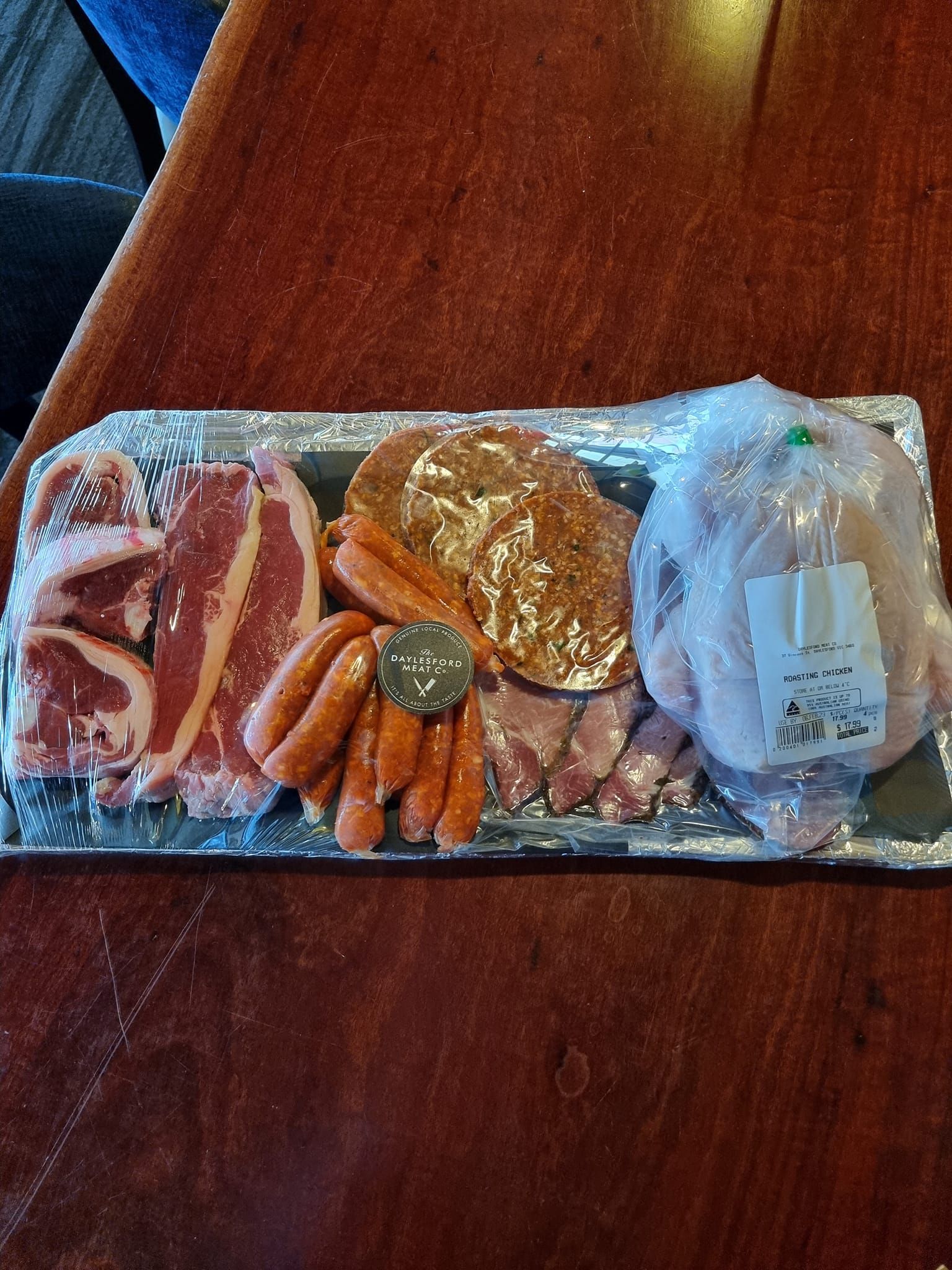 Meat tray with sausages, chops, beaf patties, bacon with cling wrap.