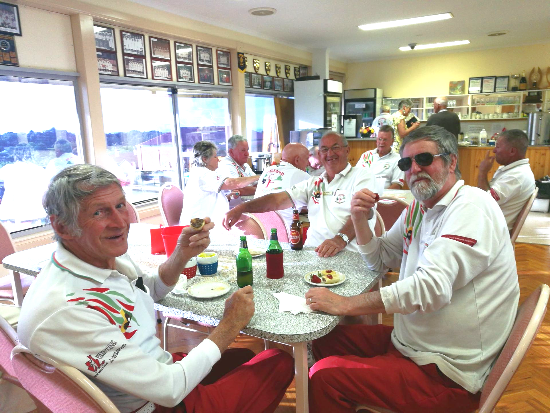 People in white and red sport uniform sitting down to a meal in club room.