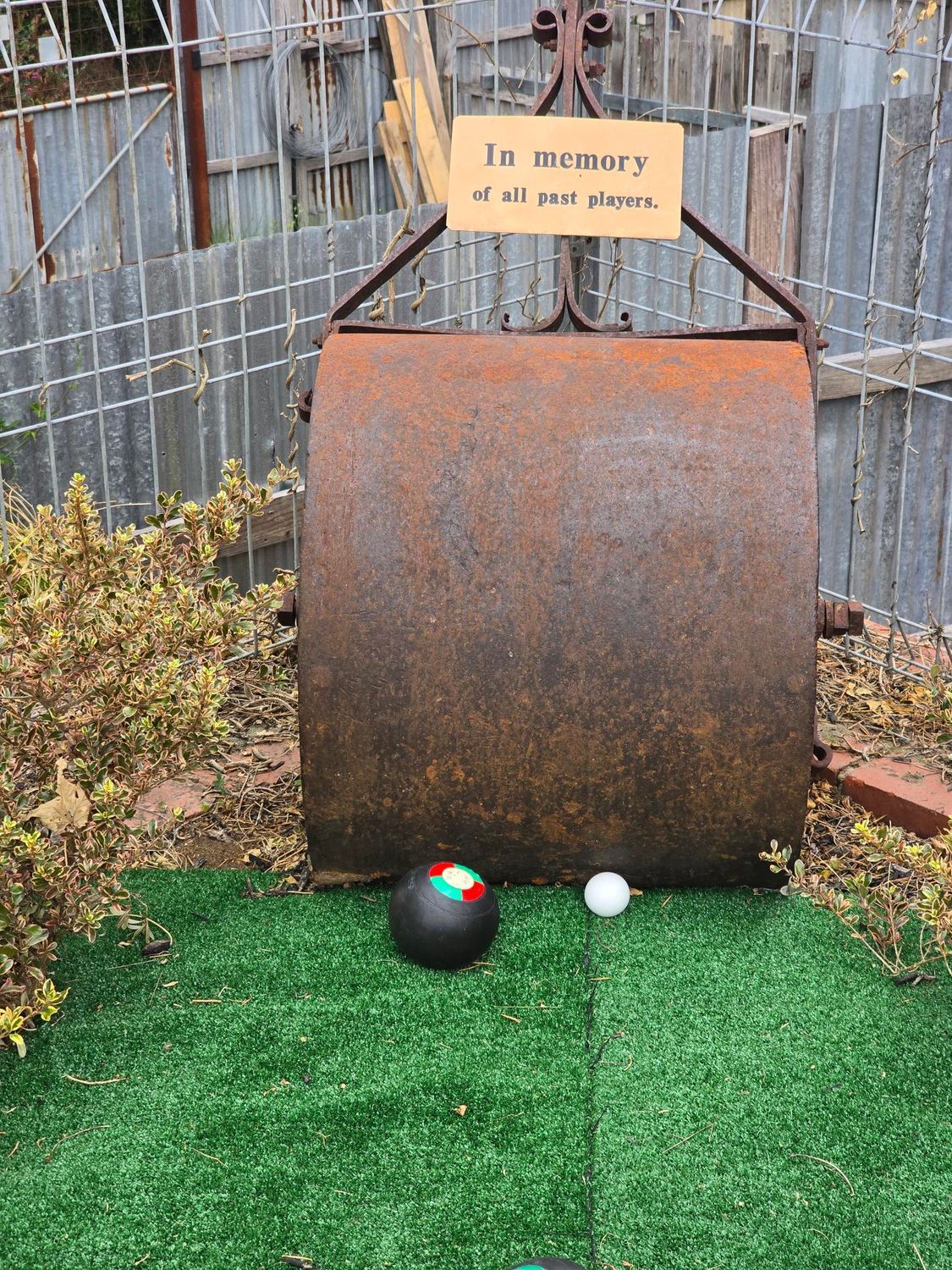 Man on ladder indoors wearing black polo shirt and shorts. Another man wearing black t-shirt and pants operating a plaster installing machine.
