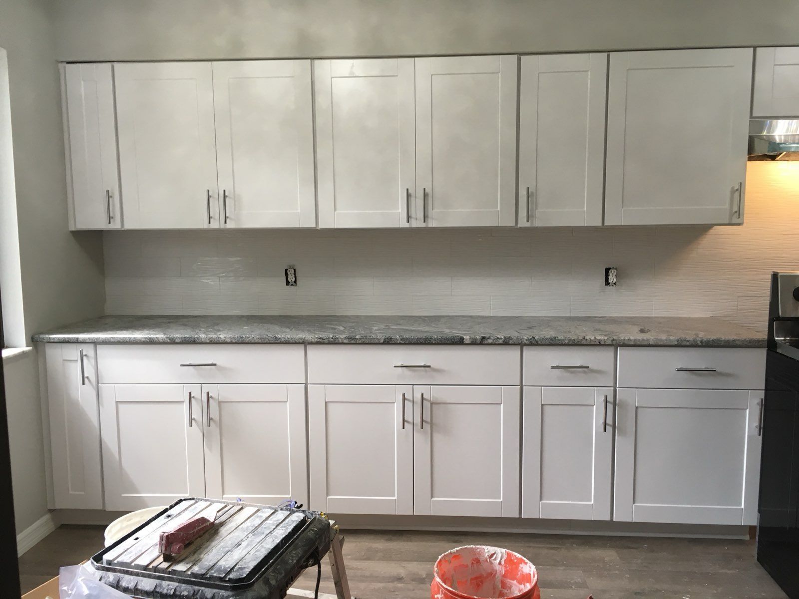 Modern white kitchen with gray countertop, upper and lower cabinets, and a small rug on the floor