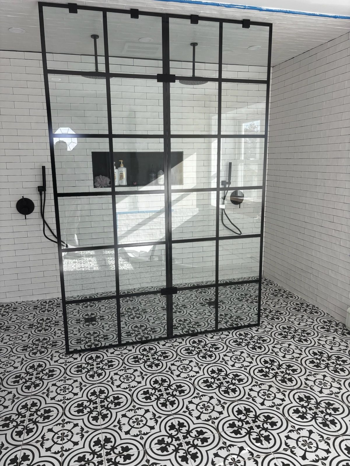 Black metal-framed glass partition in a tiled room with patterned black-and-white floor.