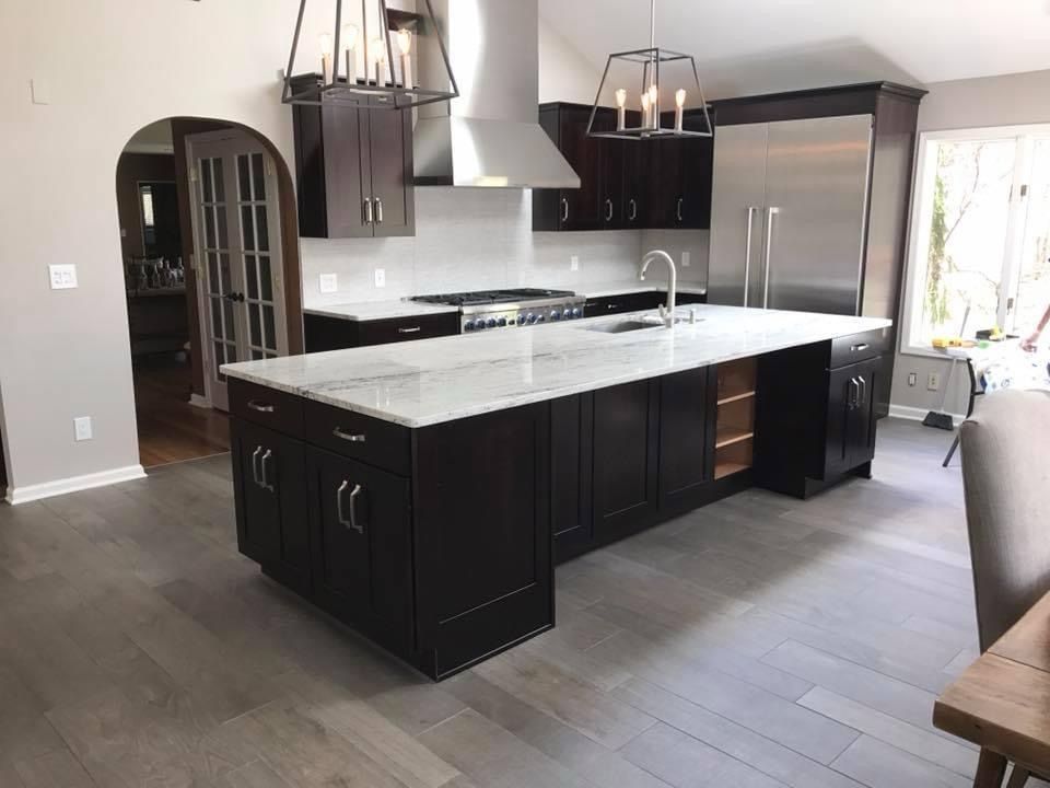 Modern kitchen with dark cabinets, large white island, stainless steel appliances, and wood-look flooring