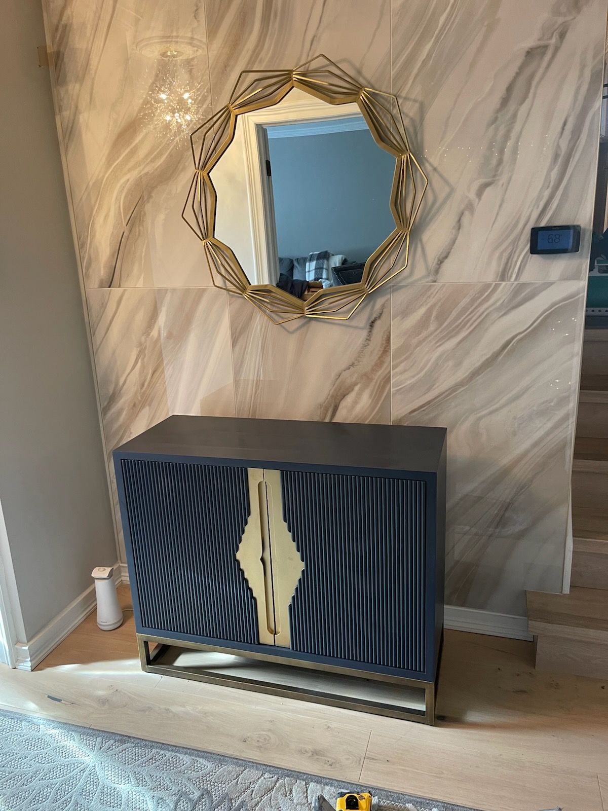 Modern console table with striped cabinet doors beneath a round decorative mirror in a marble-patterned hallway