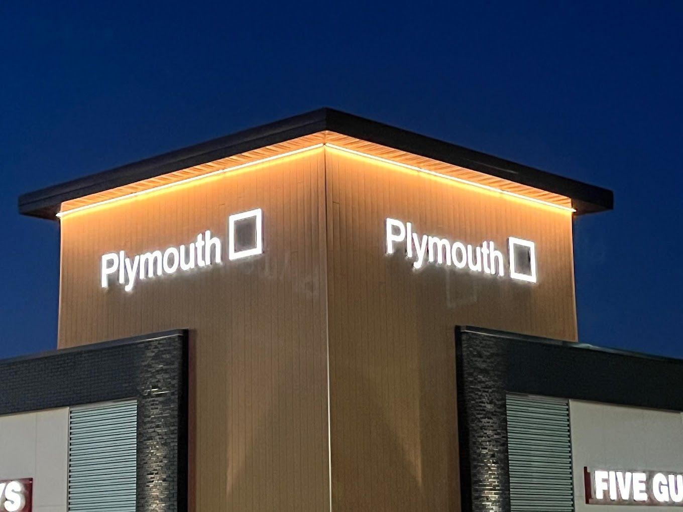 A plymouth sign is lit up at night on the side of a building