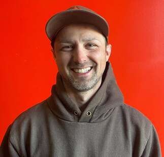 A man wearing a hat and a hoodie is smiling.