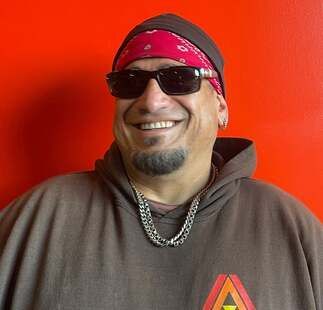 A man wearing sunglasses , a bandana and a hoodie is smiling.