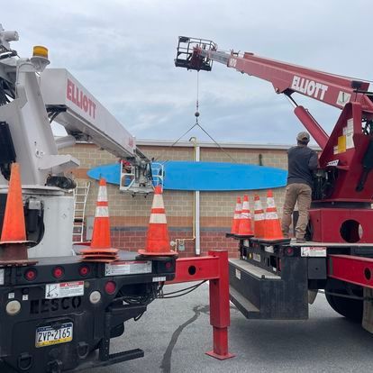 A red elliott crane is lifting a blue surfboard
