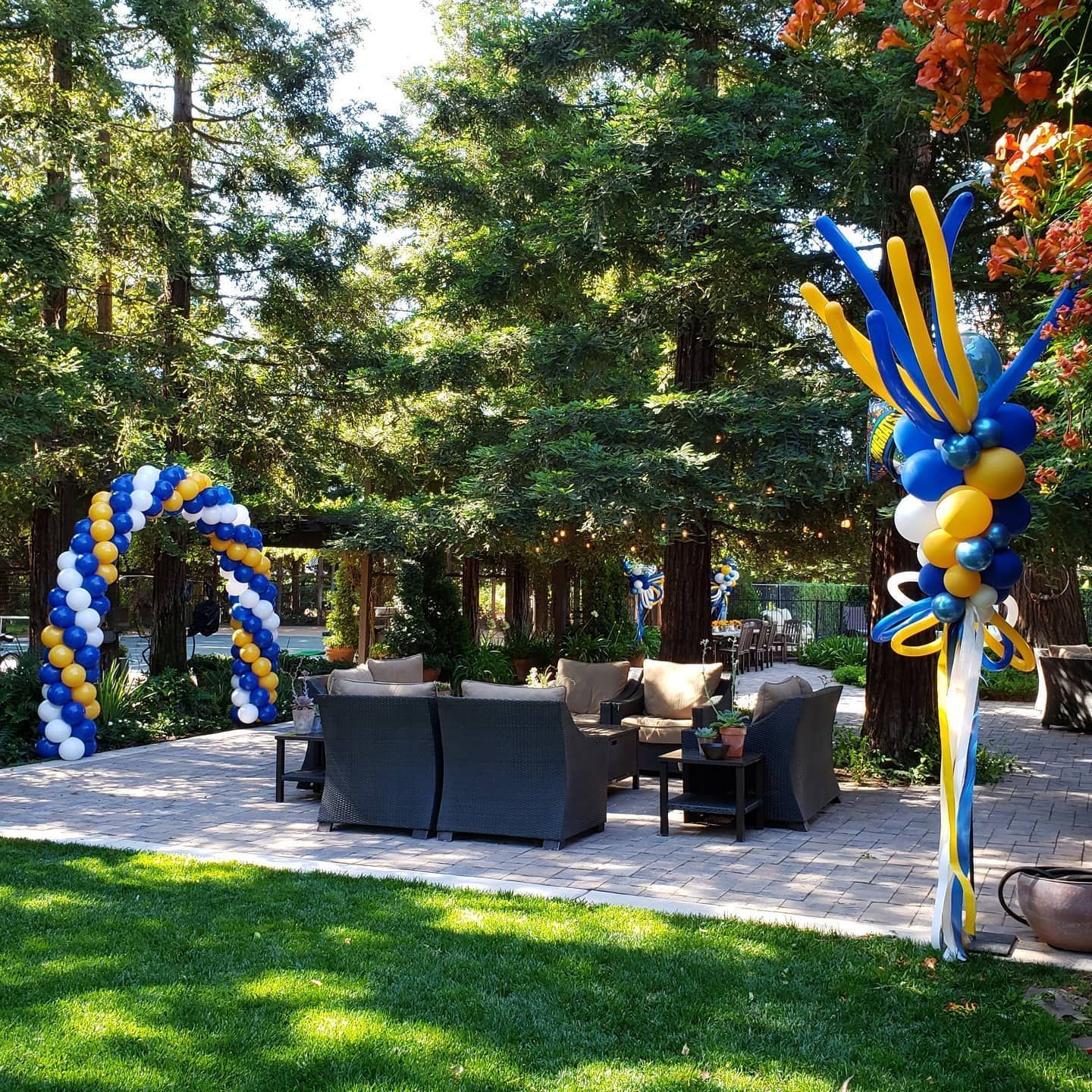 A lawn decorated with blue and yellow balloons and chairs.