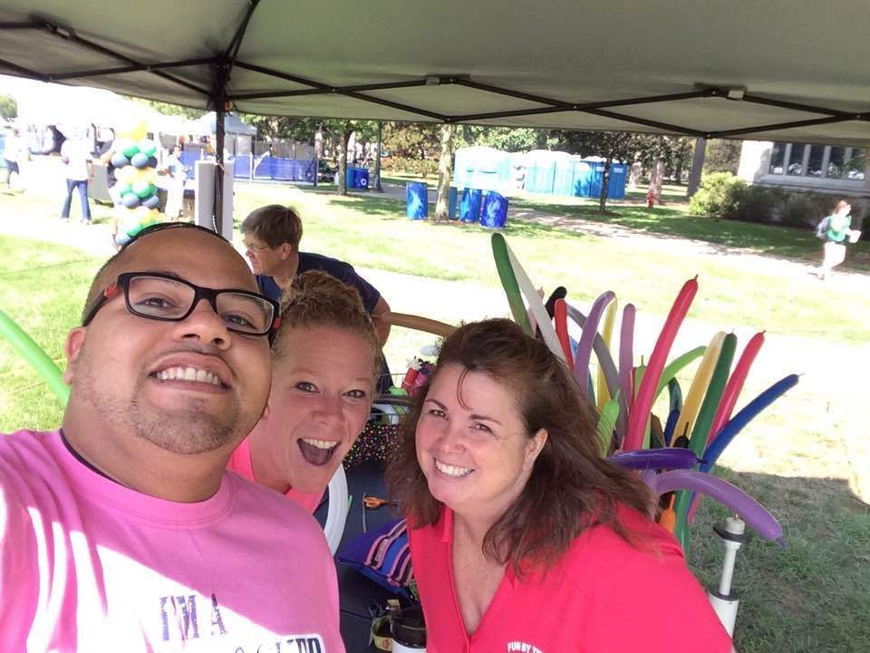 A man and two women are posing for a picture under a tent.  Balloon Twisting Entertainment