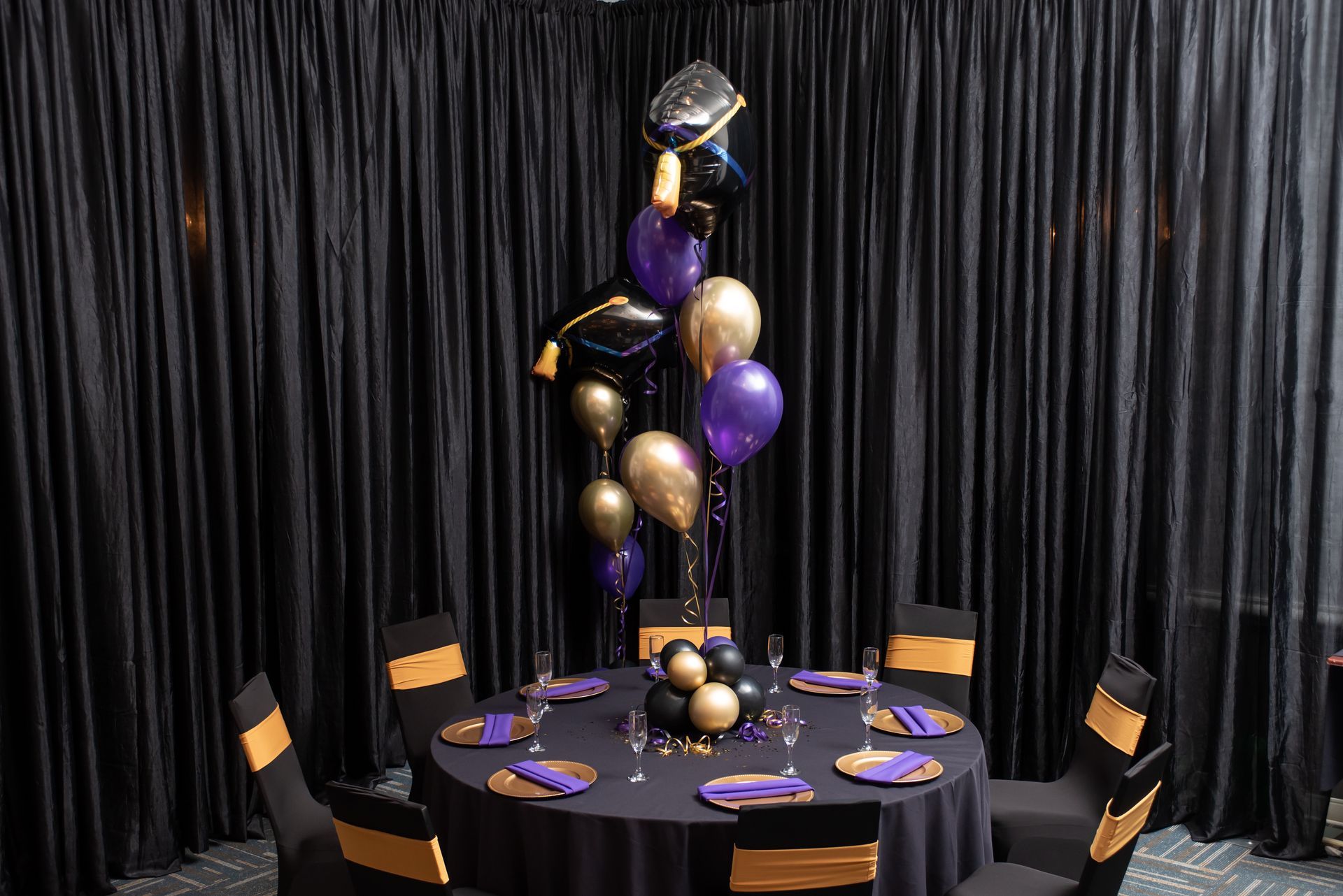 A table set for a graduation party with purple and gold balloons.