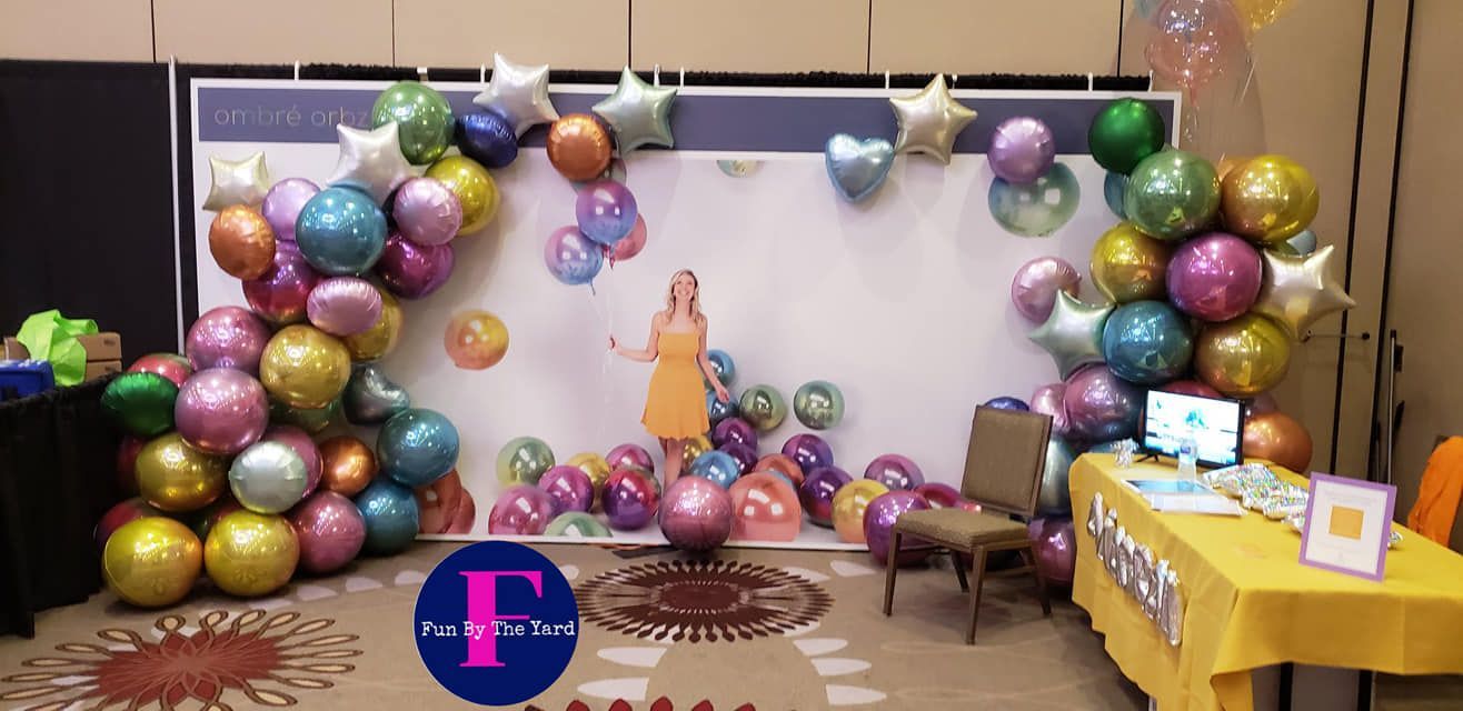 A woman is standing in front of a wall covered in balloons. Tradeshow balloons