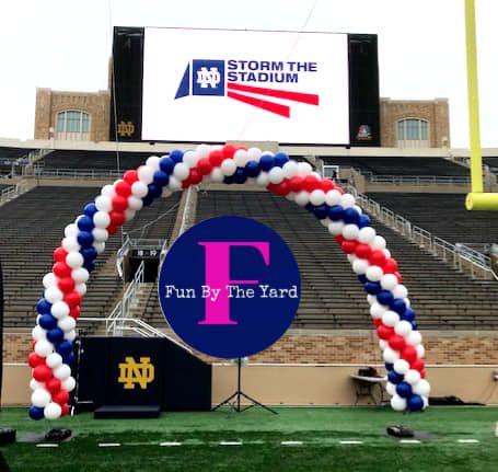 A balloon arch in front of a large screen that says storm the stadium