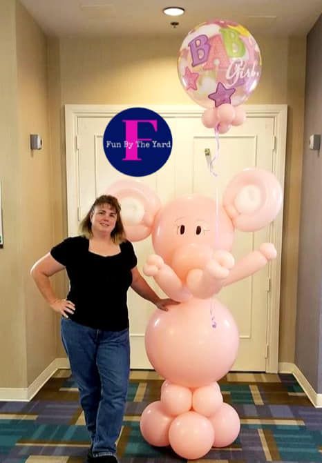 A woman standing next to an elephant made out of balloons