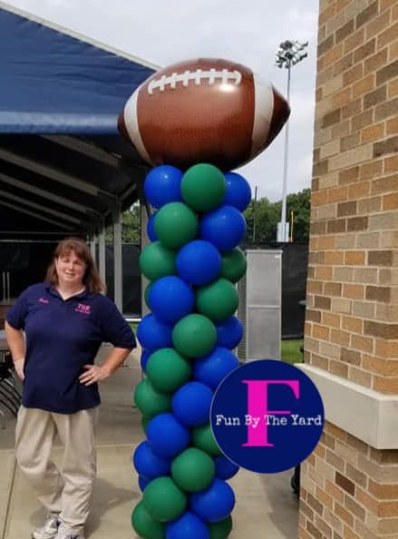 A woman stands in front of a balloon column with a football on top