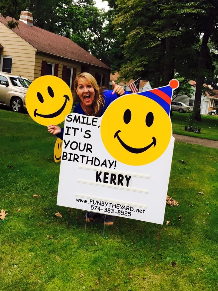 A woman holding a sign that says smile it 's your birthday kerry
