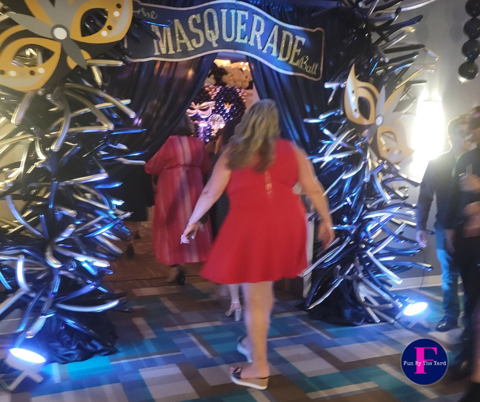 A woman in a red dress stands in front of a sign that says masquerade