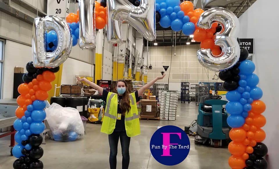 A woman in a yellow vest is standing in front of a balloon arch at Amazon