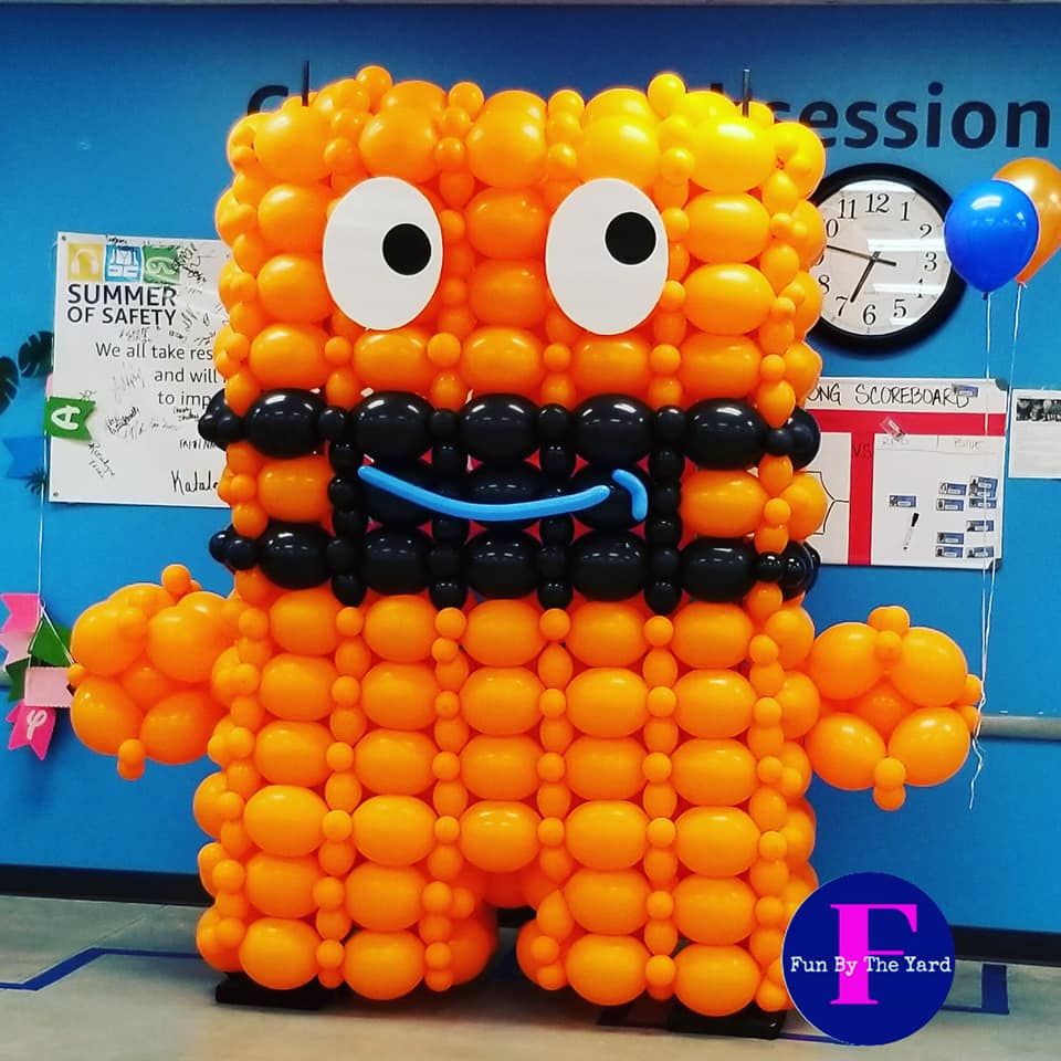 A monster made out of orange balloons is standing in front of a sign that says summer of safety