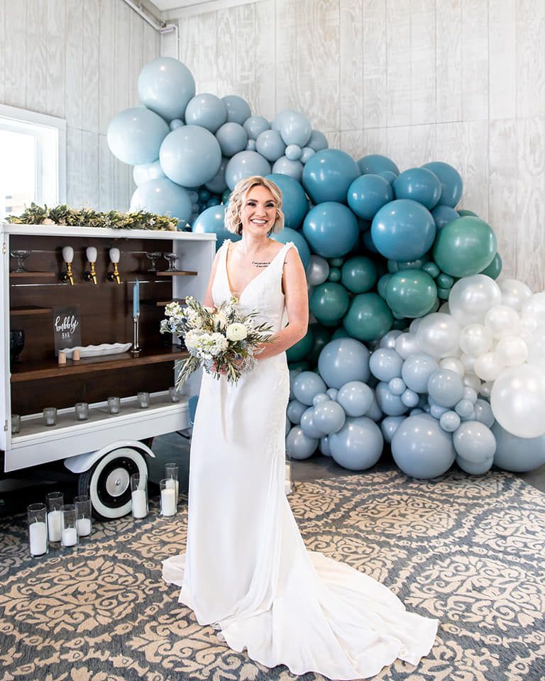 A bride in a white dress is standing in front of a wall of balloons.