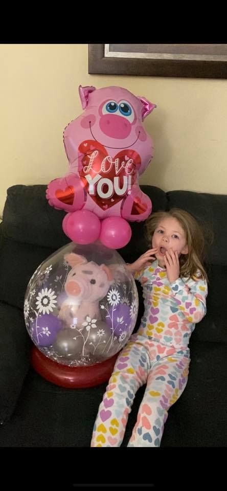 A little girl is sitting on a couch next to a stuffed pig balloon.