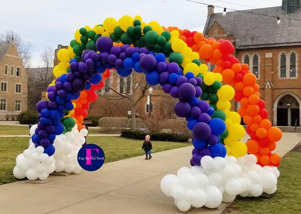 a child is walking under a rainbow made of balloons