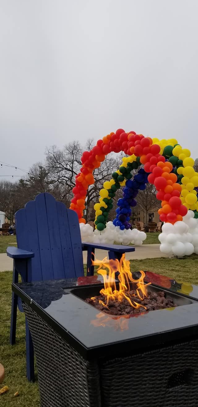 A fire pit with a rainbow balloon arch in the background.