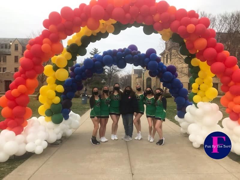 A group of cheerleaders standing under a rainbow of balloons
