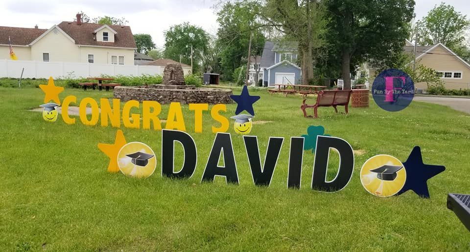 A congratulations sign for david is sitting in the grass in front of a house.