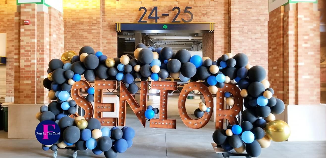 A sign that says senior is surrounded by balloons in front of a brick building.