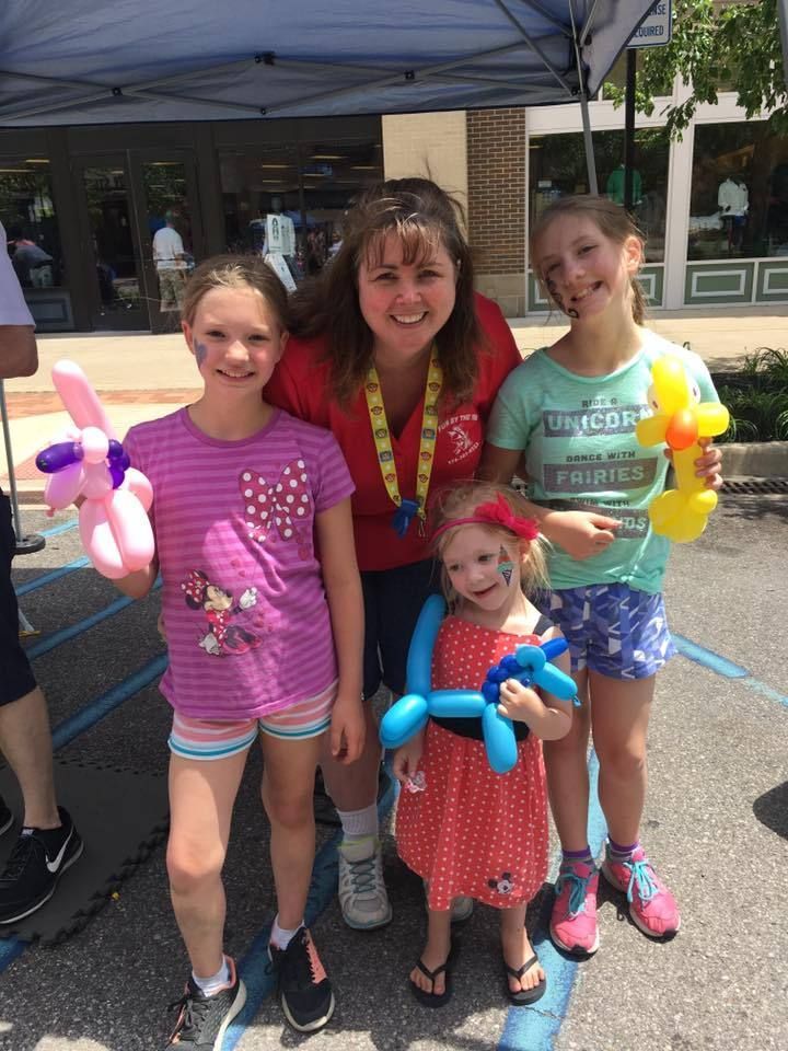 A woman is standing next to three little girls holding balloons.