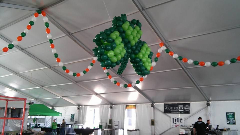 A clover made out of balloons is hanging from the ceiling of a tent.