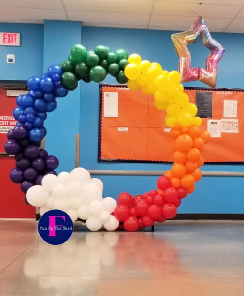 A rainbow colored balloon infinity hoop in a hallway with an exit sign in the background